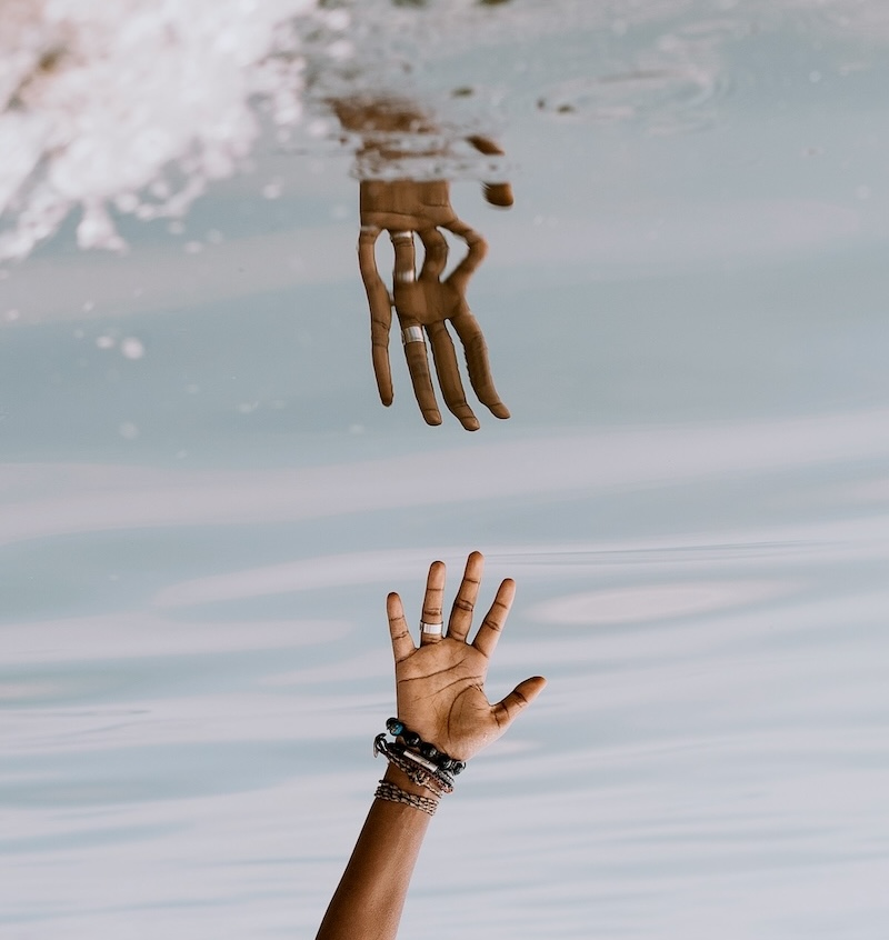 A hand reaching above the surface of calm water, partially submerged and mirrored.